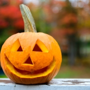 A close up shot of a happy jack-o-lantern sitting on a rail of a deck during the day