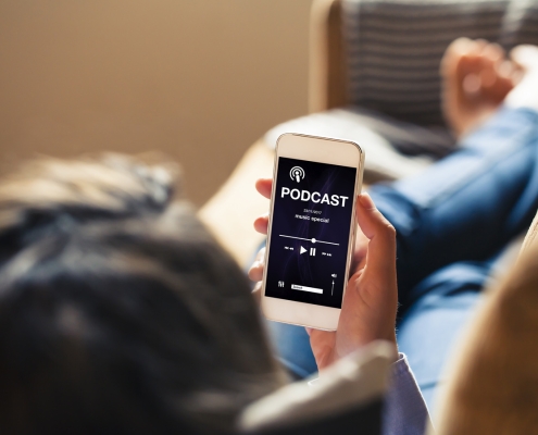 Woman at home holding a mobile phone with podcast app in the screen