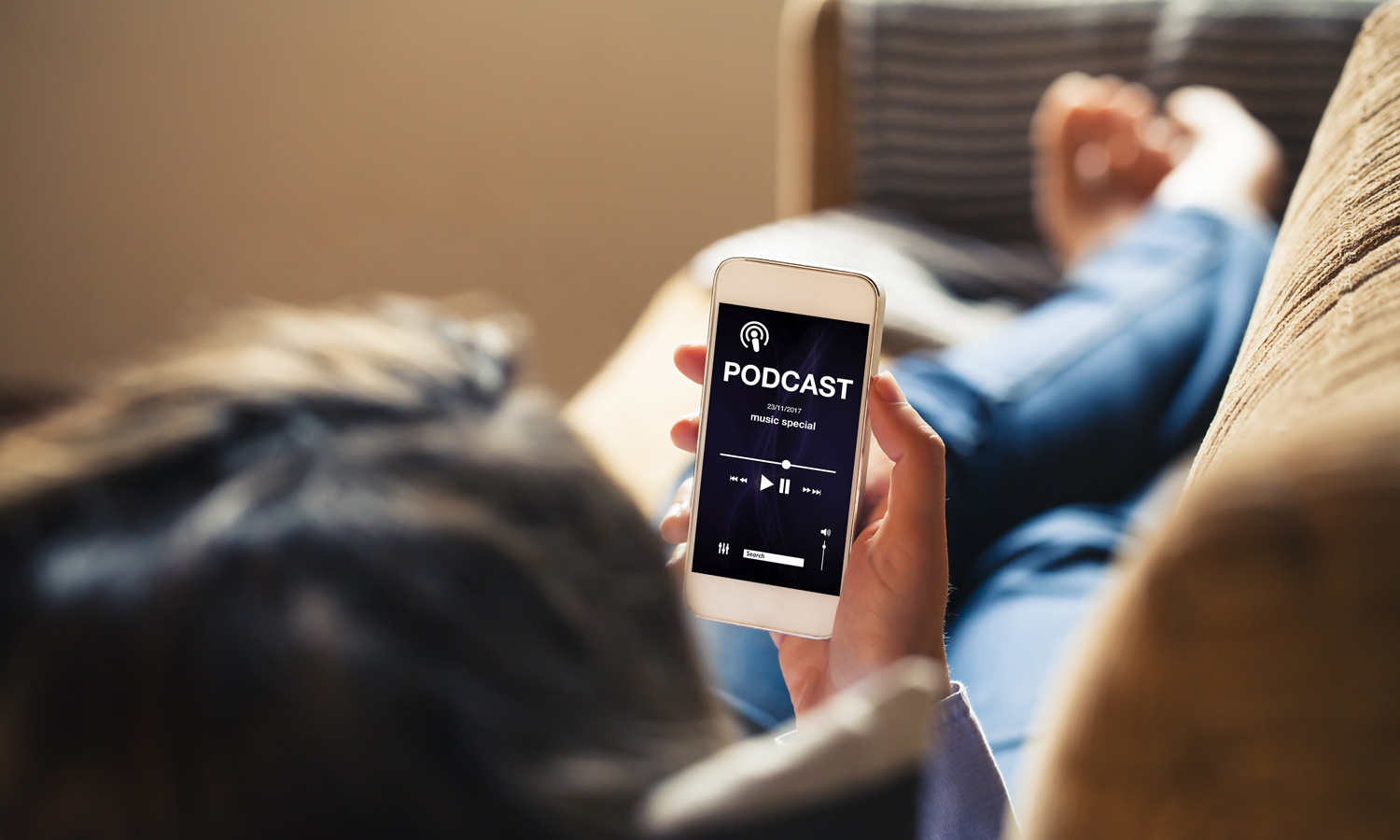 Woman at home holding a mobile phone with podcast app in the screen