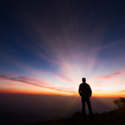 Silhouette of a man standing on the cliff looking at sunrise background, hope and following a dream concept