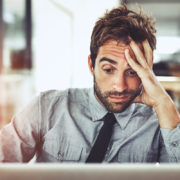 a businessman sits in front of his laptop, hand to his head in frustration or weariness